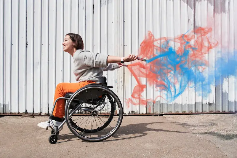 Frau om Rollstuhl vor einem Container mit Graffiti