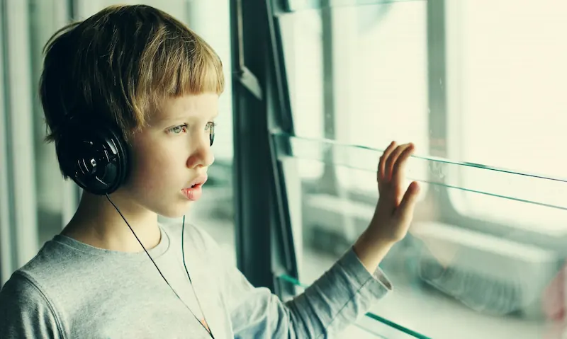 Autistisches Kind mit Kopfhörern an Glasscheibe