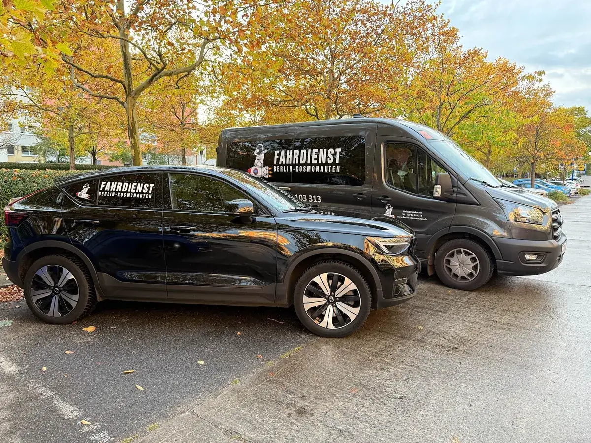 Zwei Fahrzeuge vom Fahrdienst Berlin-Kosmonauten auf einem Parkplatz im Herbst
